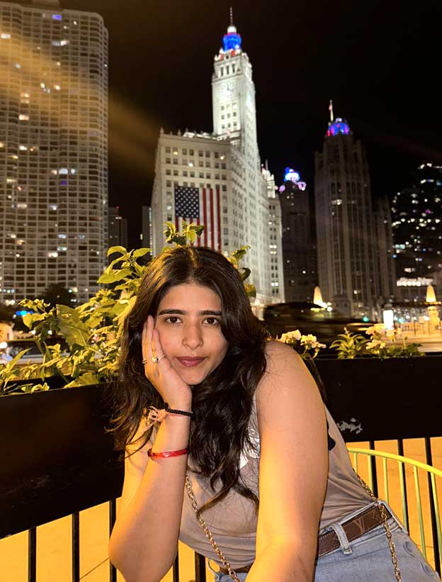 Hetshree Vyas poses in front of the city and an American flag